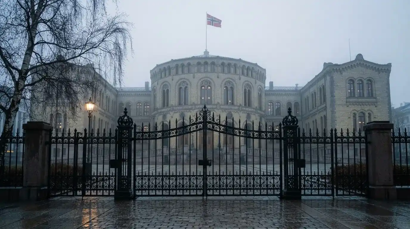 Svart jernport foran en stor offentlig bygning i stein med et flagg på stang, tåkete morgen